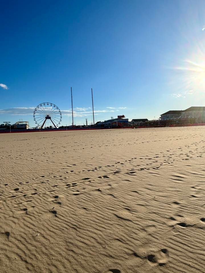 A sandy beach with a ferris wheel in the background, Ocean City MD.