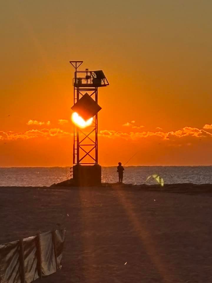 A man is standing on a beach at sunset next to a lifeguard tower.