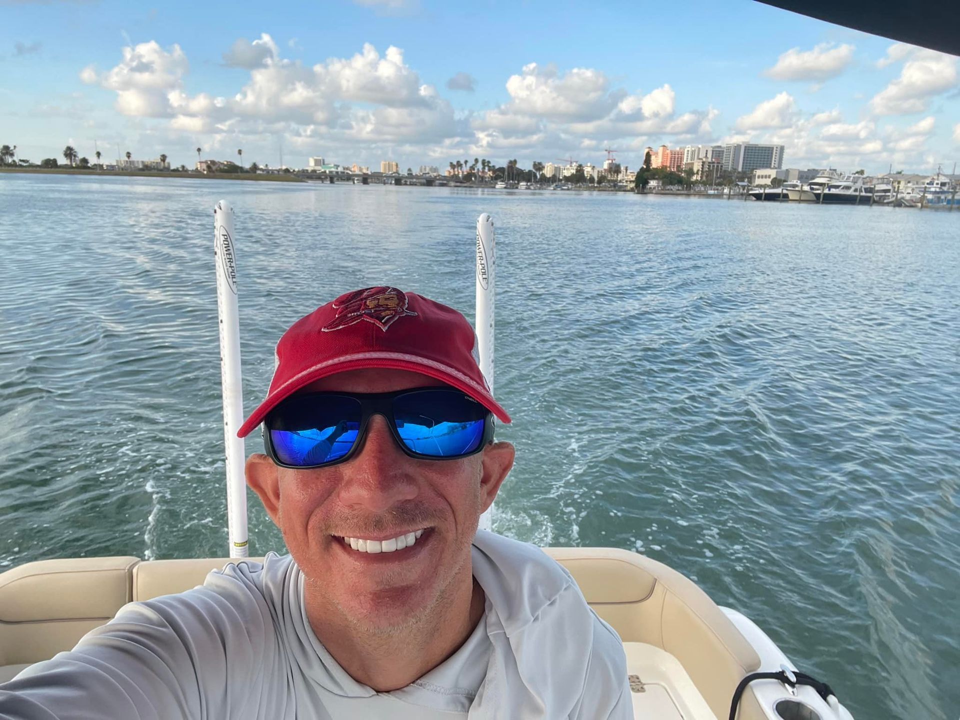 A man wearing sunglasses and a red hat is taking a selfie on a boat.