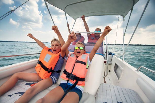 A group of children are sitting on a boat with their arms in the air.