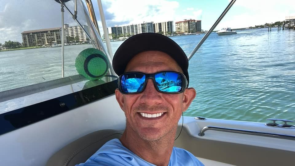 A man is sitting on a boat wearing sunglasses and a hat.