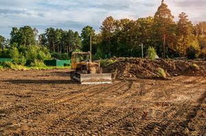 A bulldozer is moving dirt in a field with trees in the background.