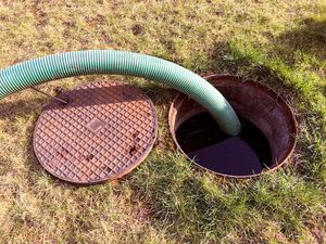 A green hose is pumping water into a septic tank.