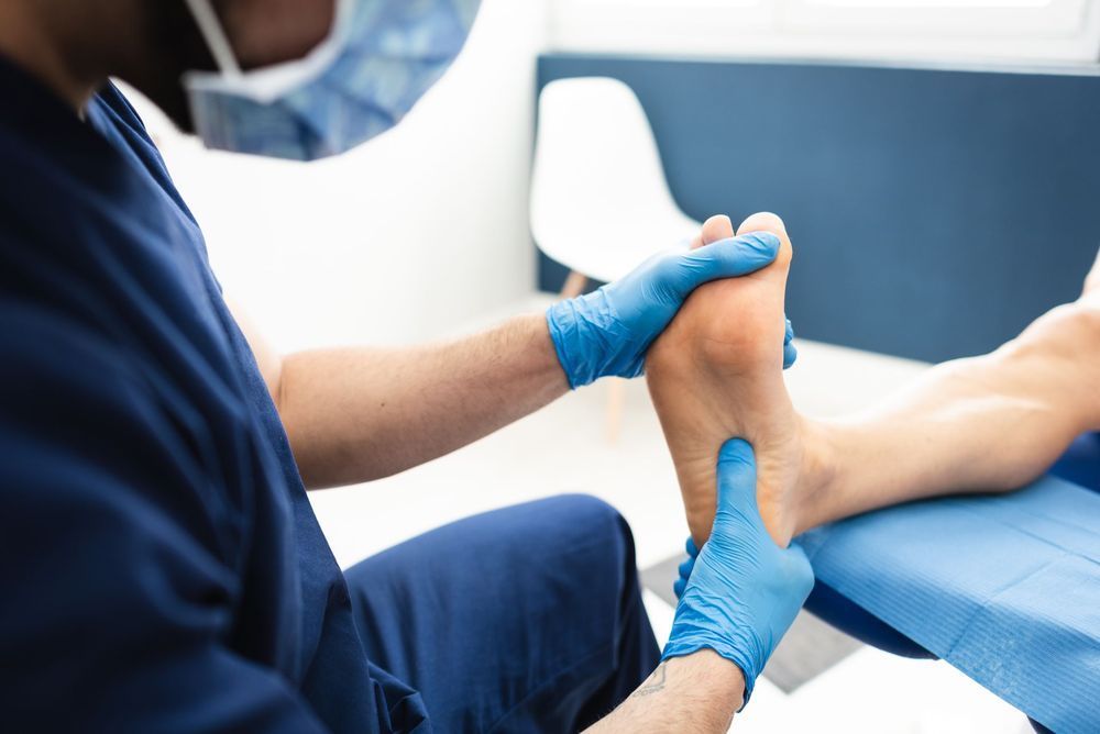 Un medico con i guanti blu esamina il piede di un paziente su un lettino da visita.
