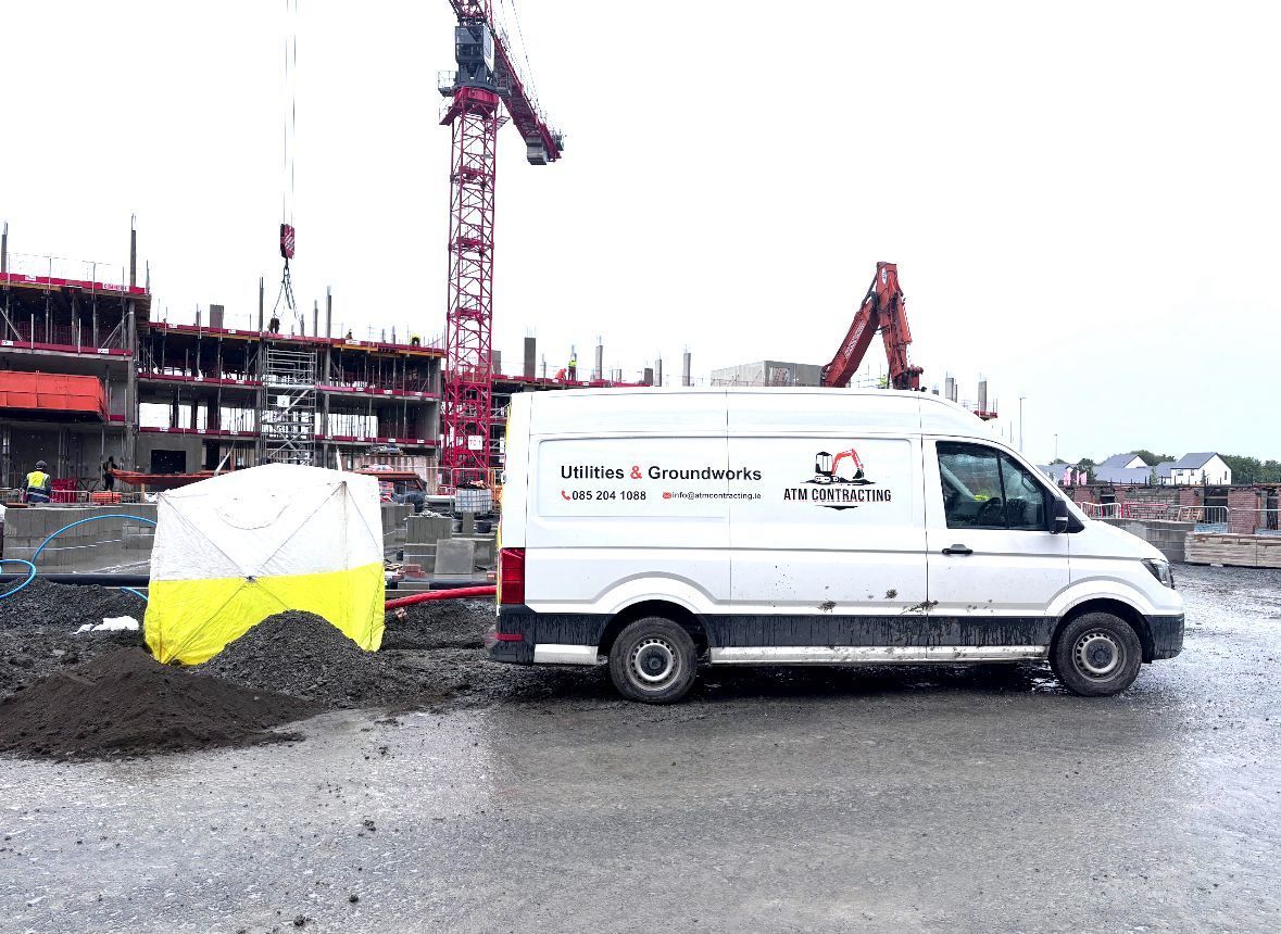 Construction site with a white van and a tent. A crane and building under construction are in the background.