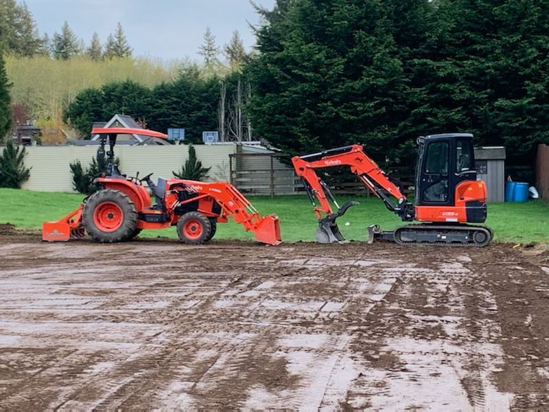 A tractor and an excavator are working on a dirt field