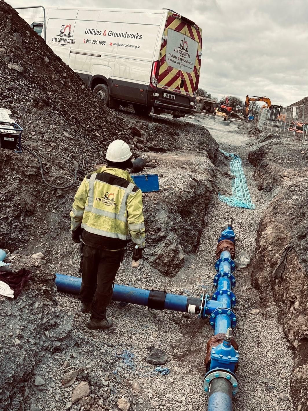 A man is standing next to a pipe in a trench.