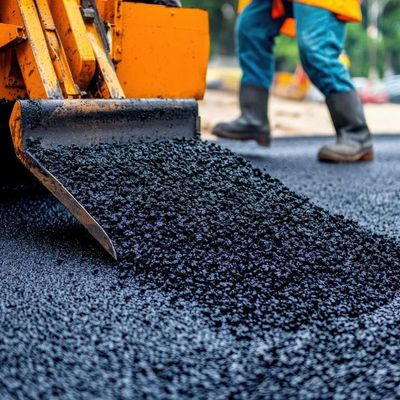A construction worker is spreading asphalt on a road with a shovel.