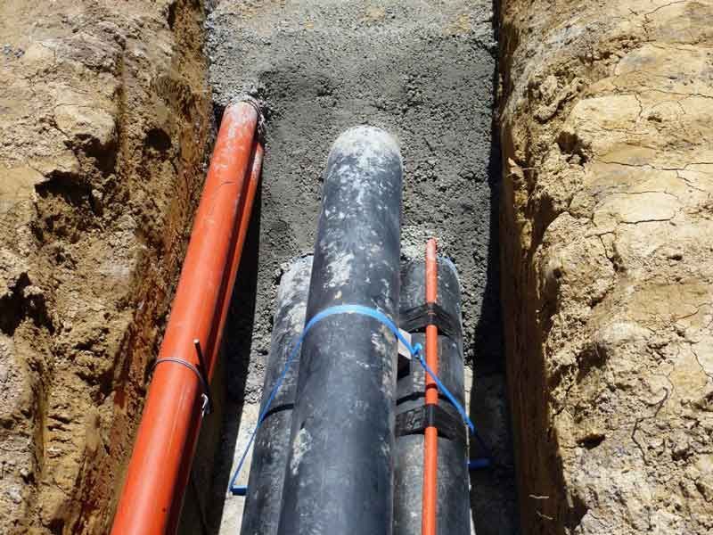 A bunch of pipes are laying in the dirt in a trench.
