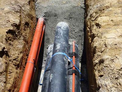 A bunch of pipes are laying in the dirt in a trench.