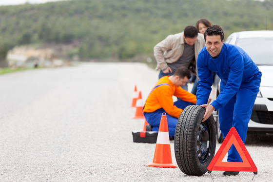 A group of men are changing a tire on the side of the road.