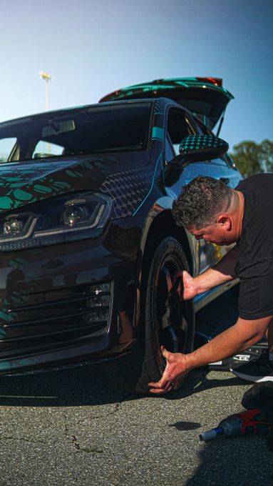A man is changing a tire on a black car.