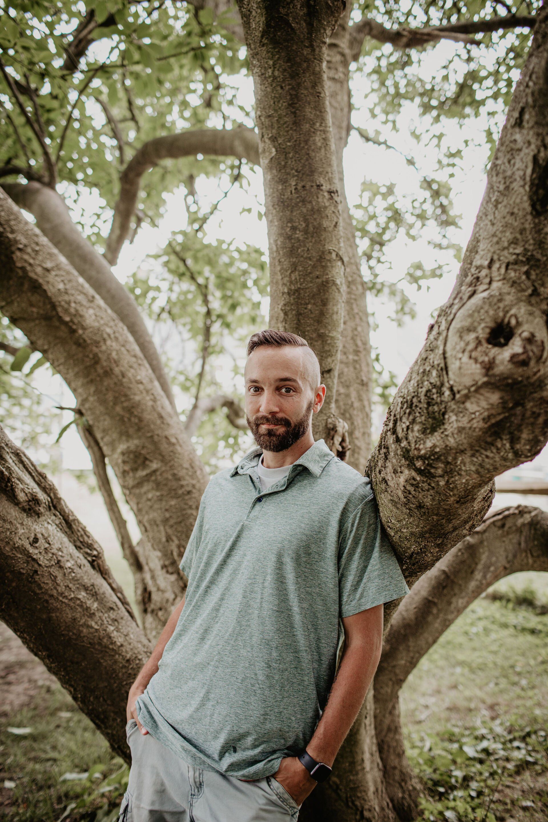 A man with a beard is leaning against a tree.