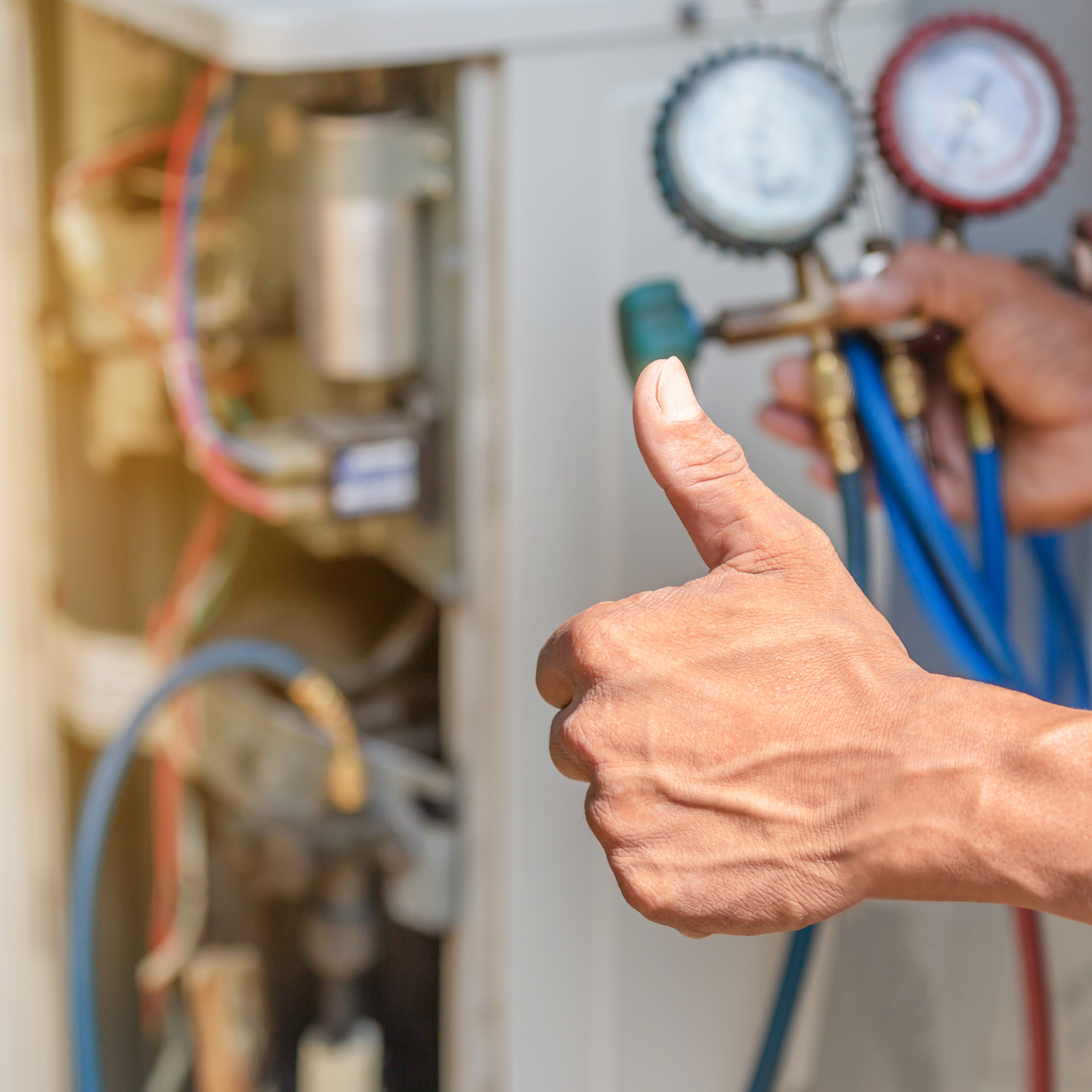 Hand holding gauges connected to an air conditioning unit, giving a thumbs up.