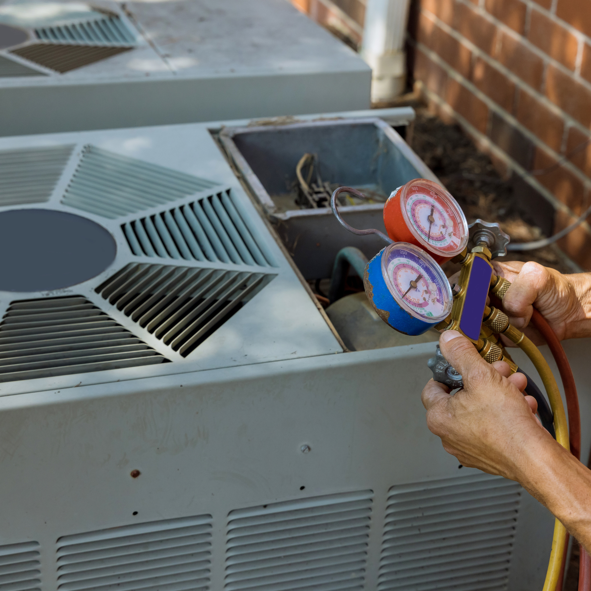 AC unit being serviced with gauges, outdoors.