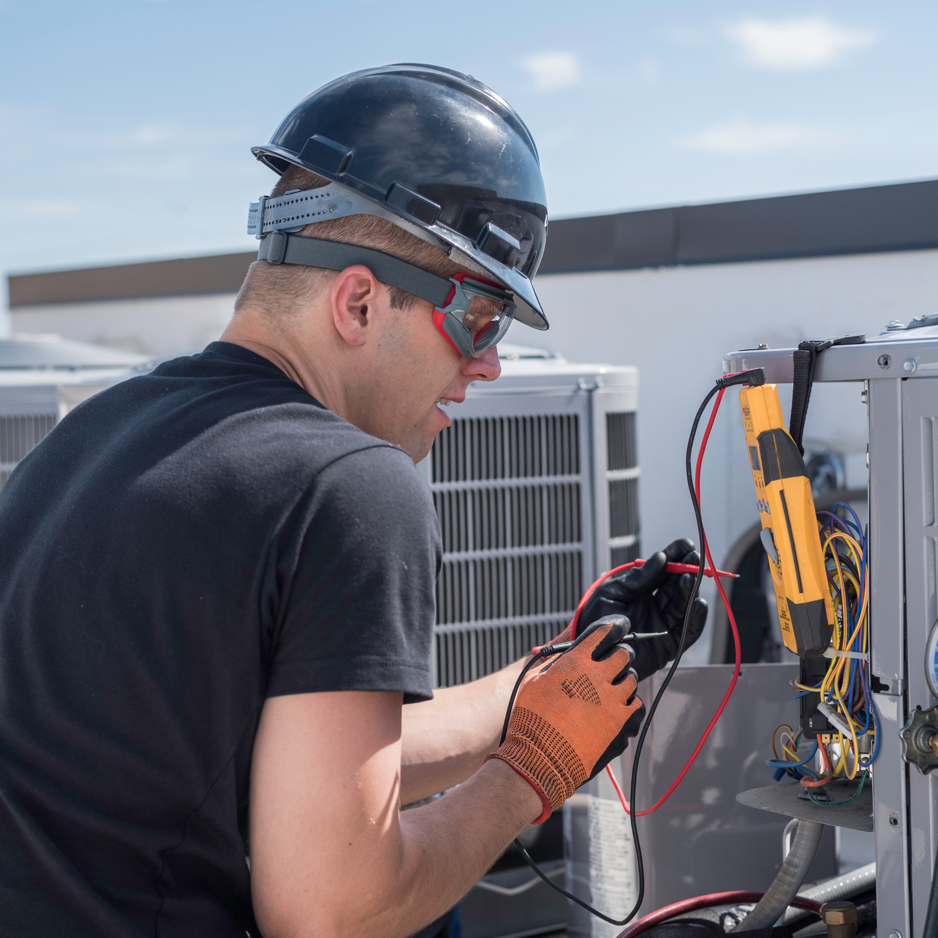 HVAC technician using a multimeter on an air conditioning unit on a rooftop.