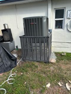 An air conditioning unit encased in a gray cage sits on gravel beside a building.