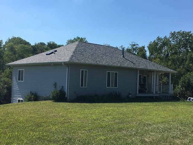 A house with a gray roof is sitting on top of a lush green field.