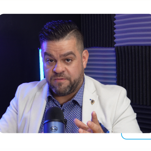 Um homem com barba está sentado em frente a um microfone.