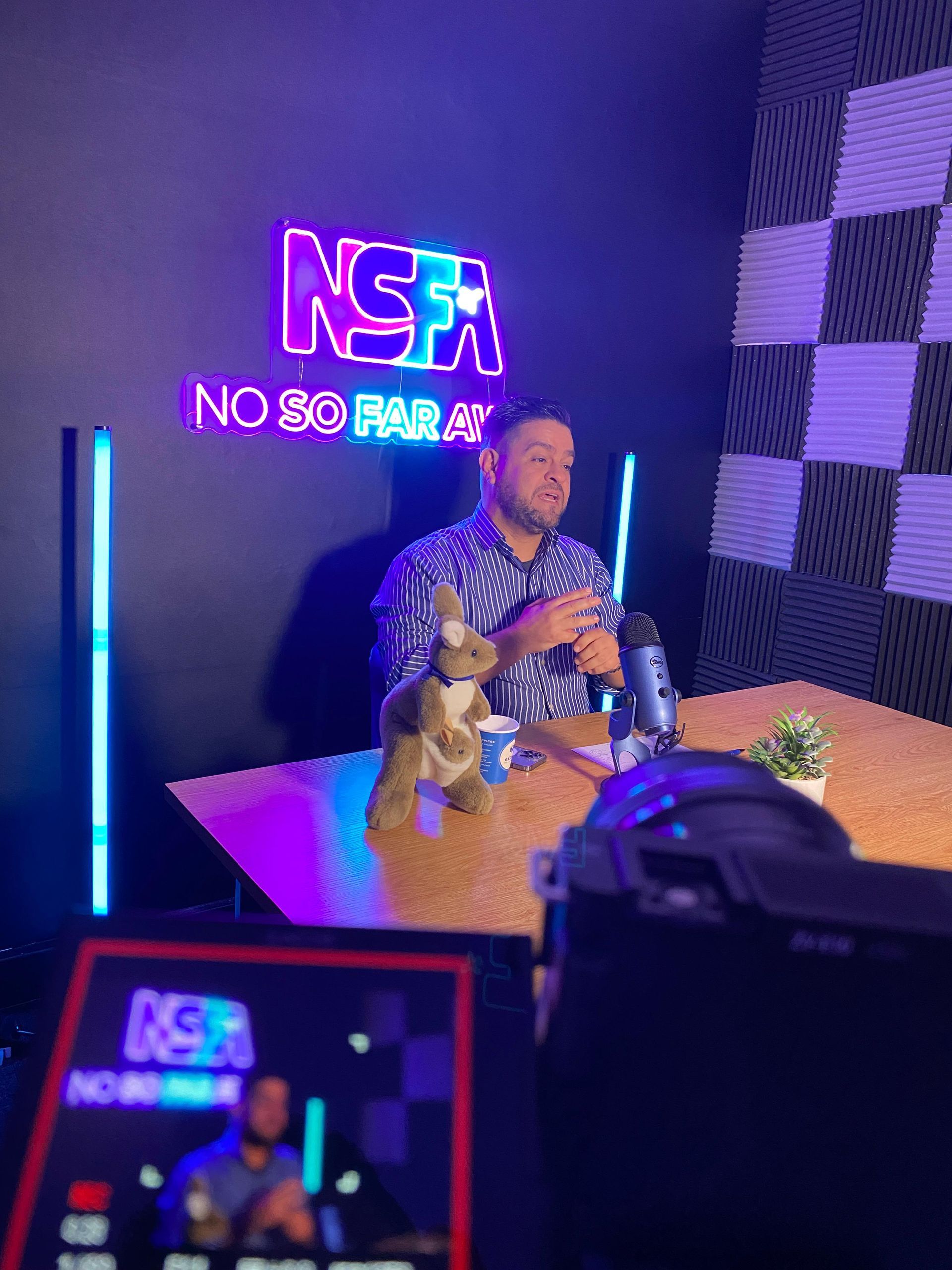 Um homem está sentado à mesa com um bicho de pelúcia na frente de um microfone.