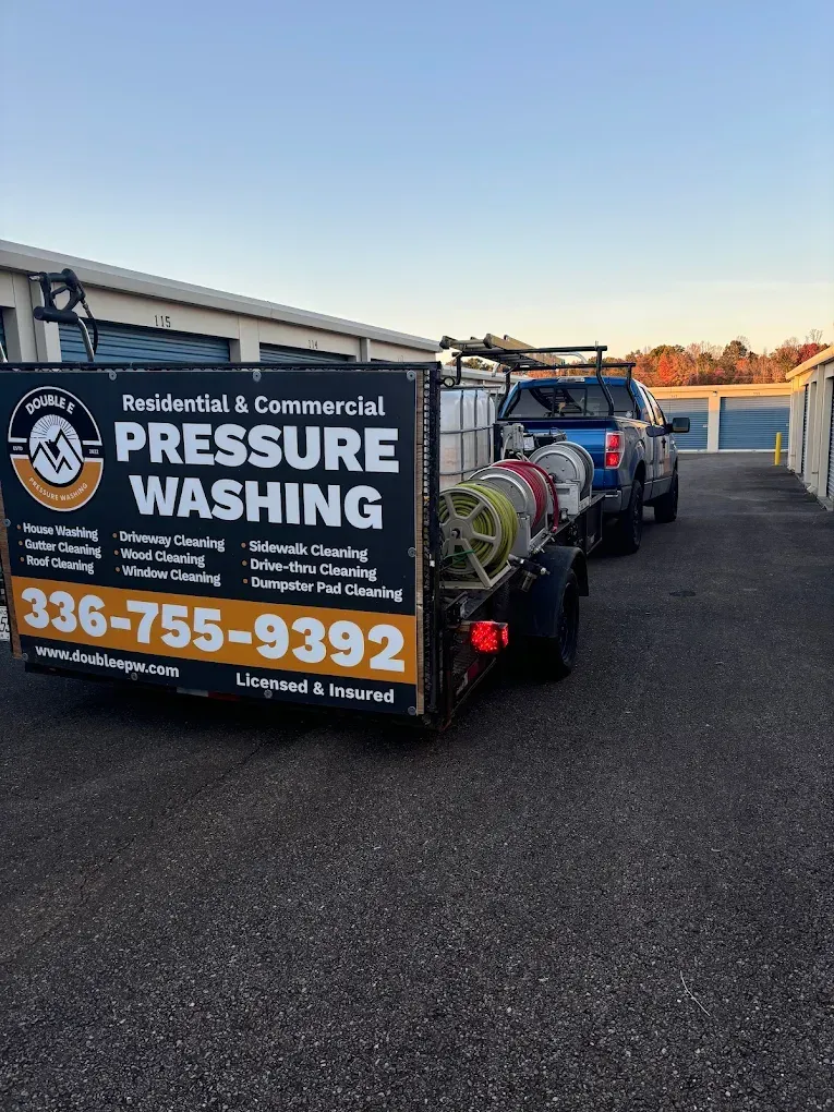 Pressure washing trailer with business logo and contact info parked in front of storage units.