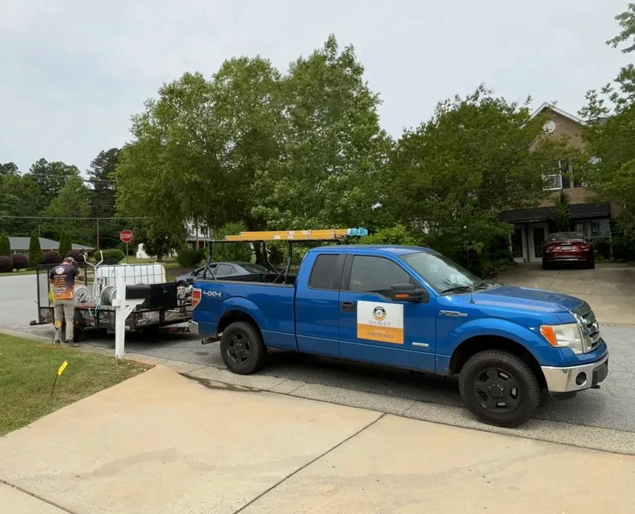 Blue pickup truck with trailer parked on driveway, utility worker near trailer.