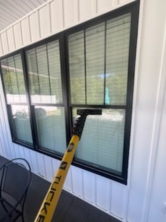 A person cleaning a window with a yellow Tucker pole. The window is black-framed and on a white building.