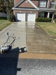 Man power washing a two-story house with brick and siding, spraying the trim.