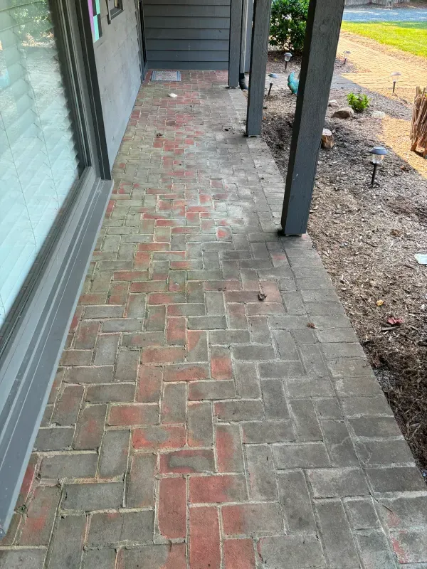 Brick walkway on a porch, with alternating red and gray bricks. Porch has a window and dark column.