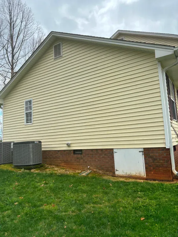 Yellow house siding, brick foundation, air conditioning units, and a door on a cloudy day.