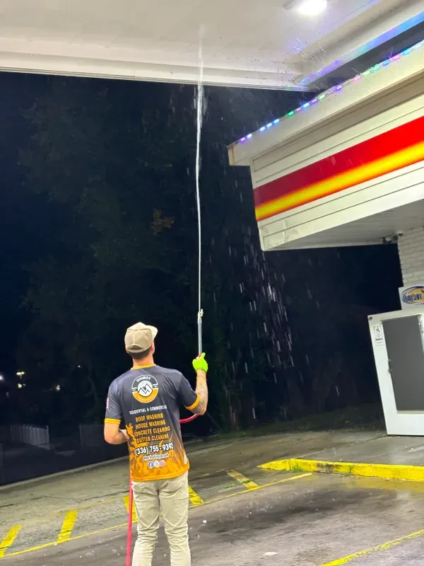 Man spraying water towards the canopy of a gas station at night.