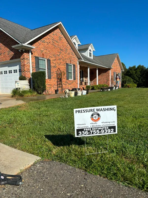 Pressure washing sign in front of a brick house. Green lawn with pots. Sunny, blue sky.