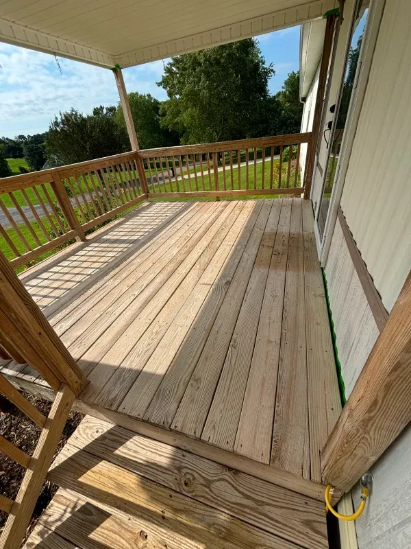Wooden deck with a railing and partial covering, attached to a house with a green door trim.