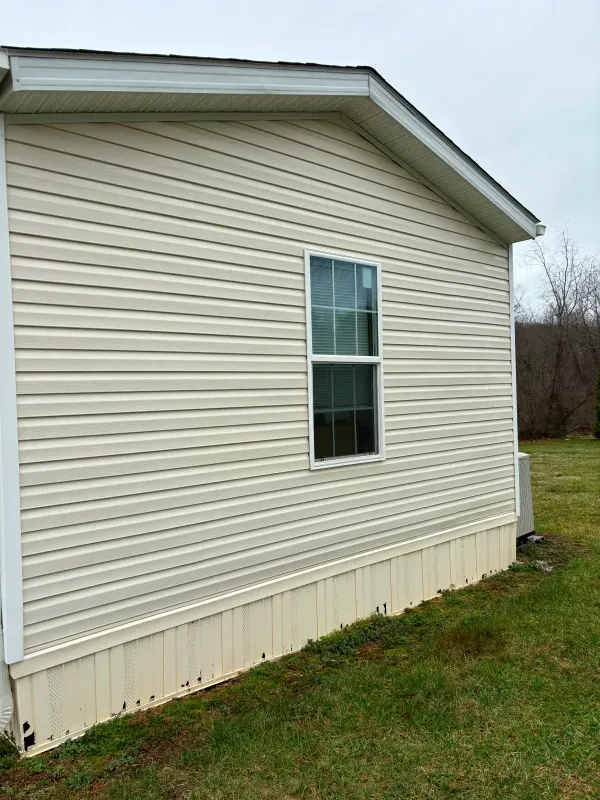 Side view of a house with cream-colored siding, a window, and a green lawn.