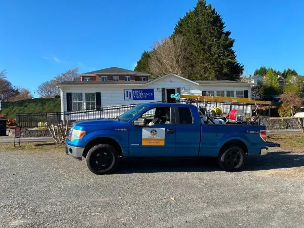 Blue pickup truck parked in front of a white building with a wheelchair ramp. Sunny day.