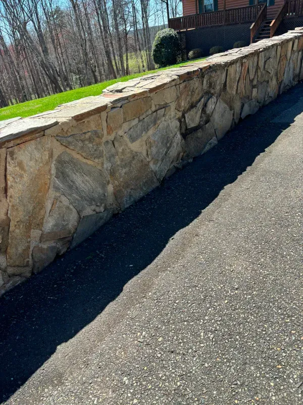 Stone retaining wall along a paved driveway, with green grass and trees in the background.