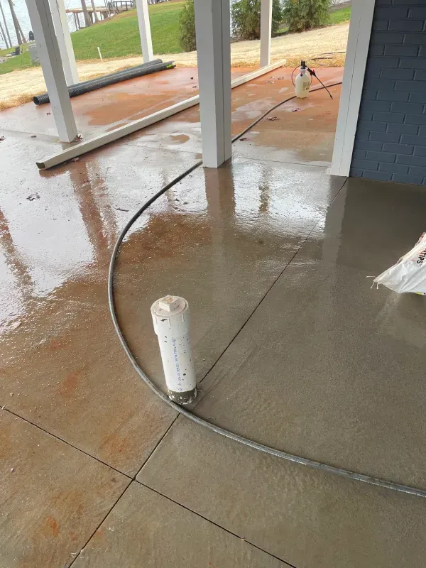 Wet concrete patio being finished with a curved border, includes a white pipe and pillars.