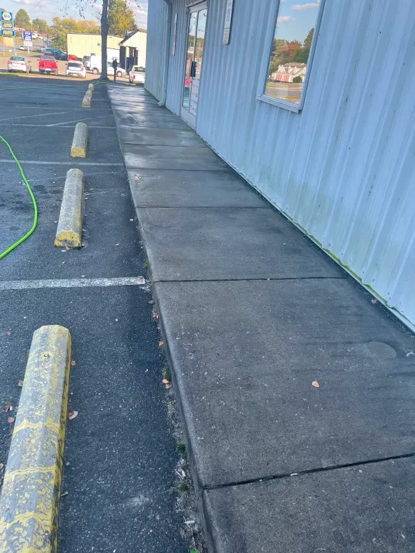 Sidewalk adjacent to a building being pressure washed; yellow parking stops in view.