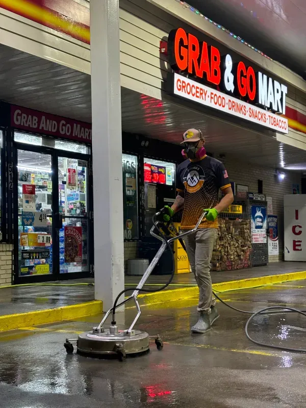 A person power washes the ground in front of a convenience store called 