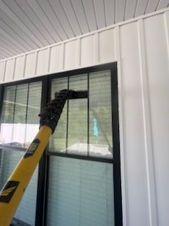 Cleaning a window with a long-handled tool; white siding and a black window frame are visible.