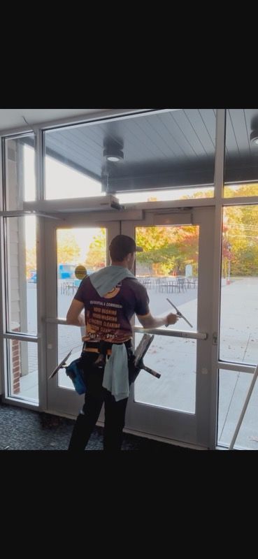 A person cleans windows in a building. The person is wearing work clothes and using a squeegee.