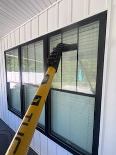 Man power washing a two-story house with brick and siding, spraying the trim.