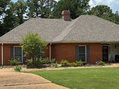 Red brick house with gray roof, green lawn, trees, and chimney.