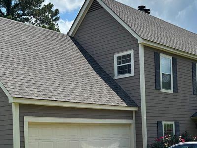 Two-story house with gray siding, a garage door, and a gray roof against a cloudy sky.