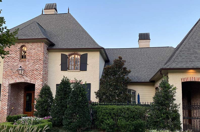 Elegant two-story house with a brick facade, gray roof, and manicured landscaping under a clear sky.