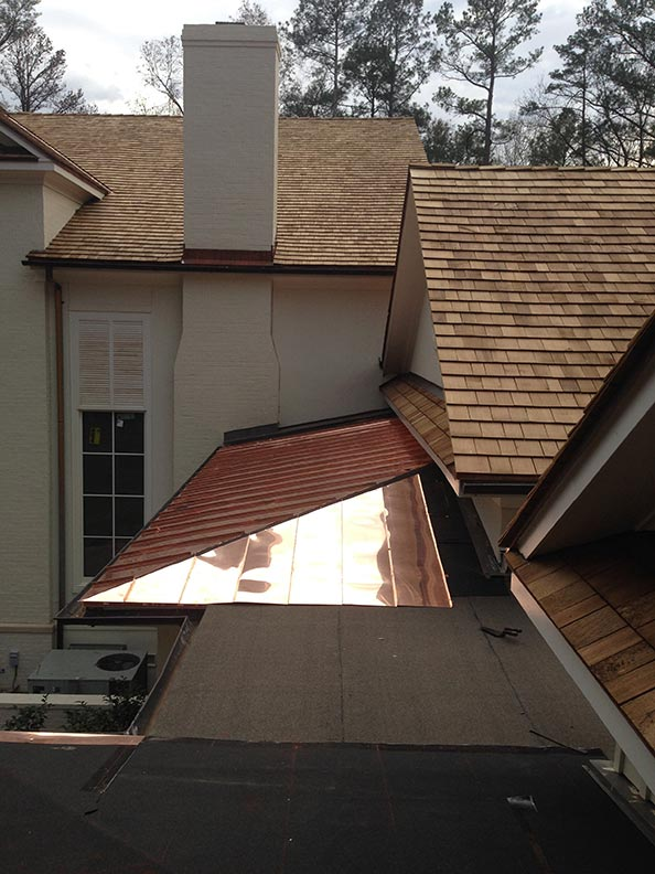 Copper roof section with cedar shake roof, white wall, and chimney.