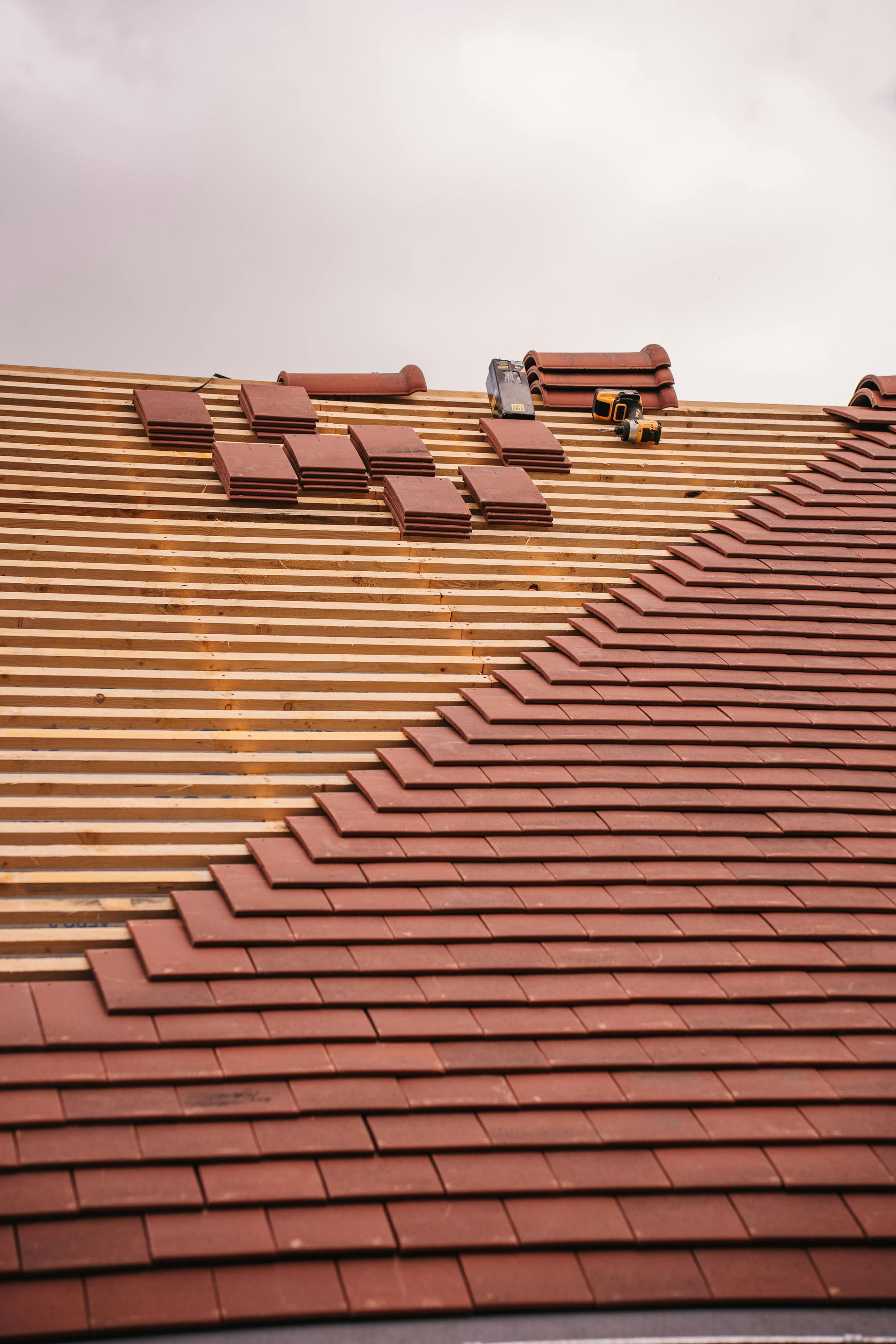 Roof partially covered with red tiles, other section bare with wooden beams. Overcast sky.