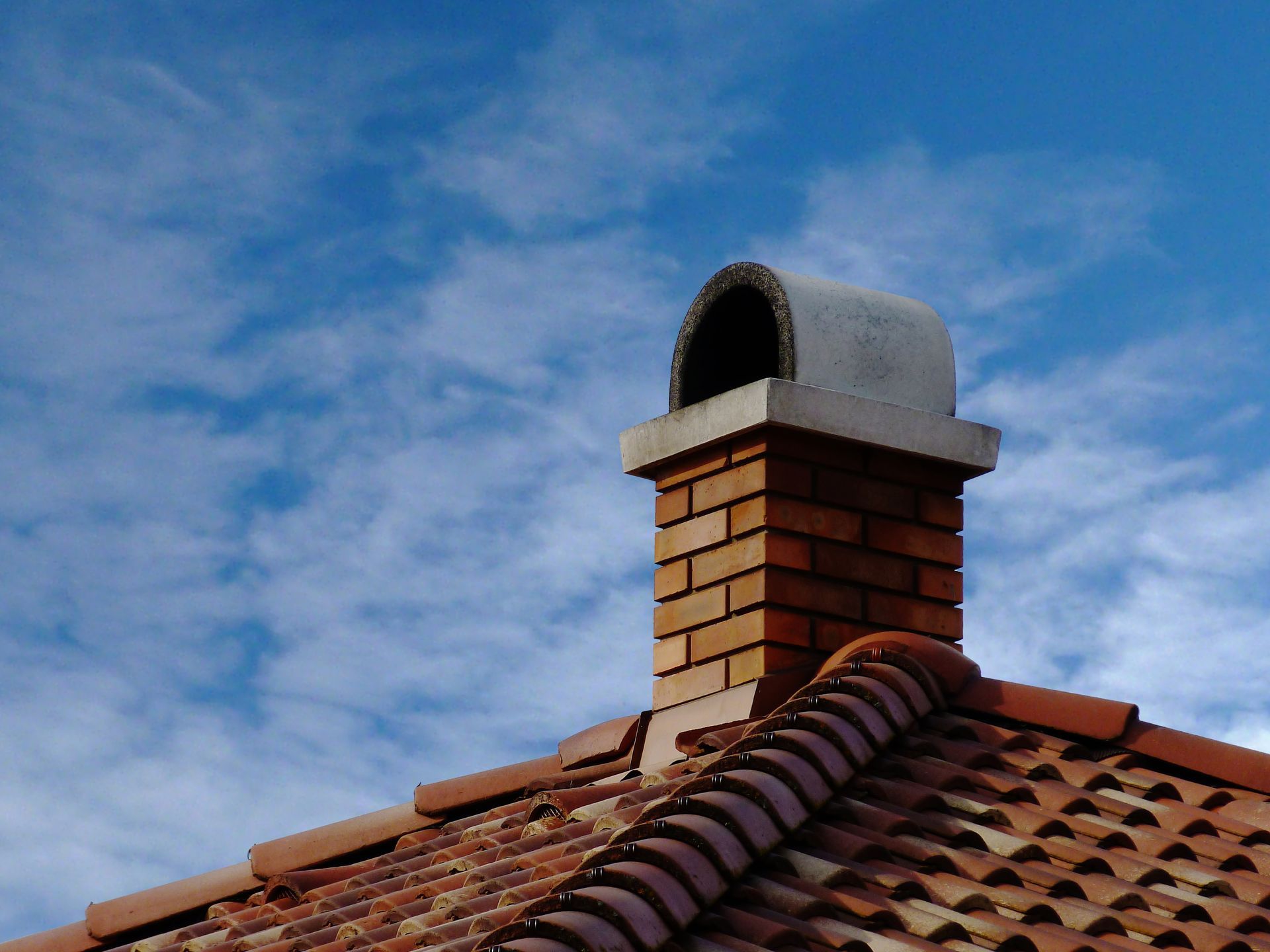 Brick chimney on a tiled roof against a blue sky with scattered clouds.
