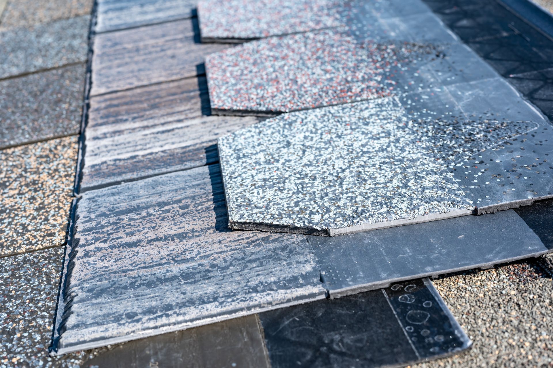 Hexagonal grey and speckled roof shingles arranged in overlapping rows on a dark underlayment.