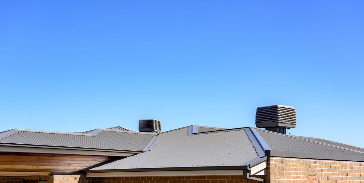 Gray metal roof on a brick building against a bright blue sky.